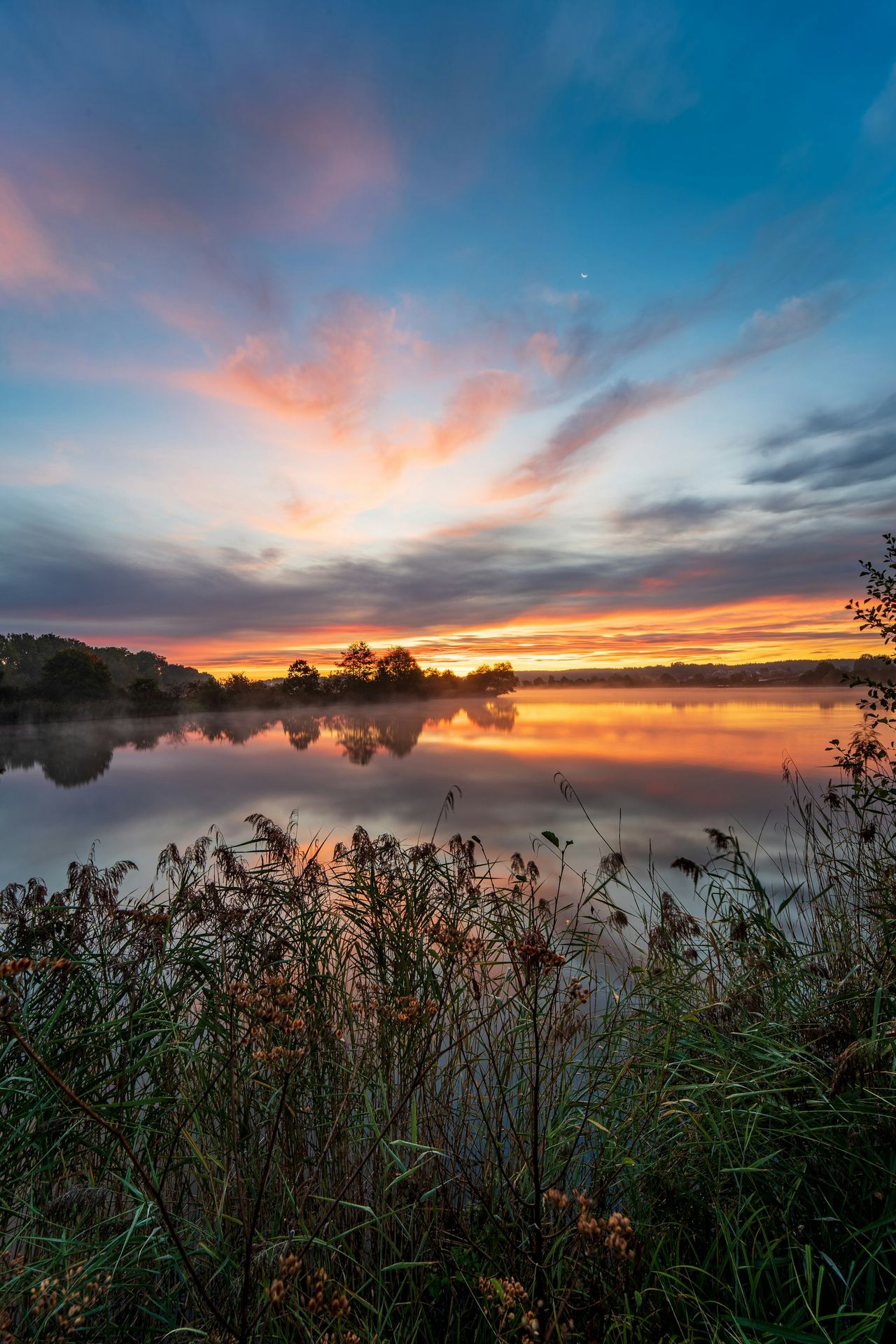 the sun is setting over a lake with trees in the foreground